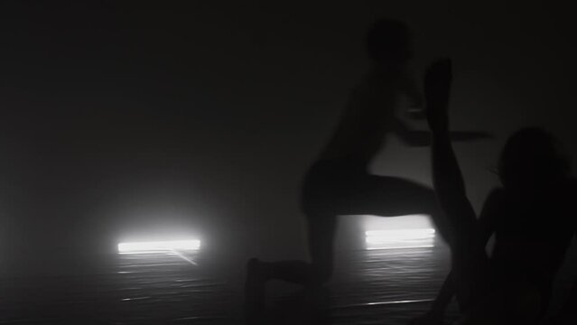 Modern ballet dancers performing together on dark stage. Silhouette of couple of performers with smoke in the air.