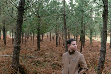 Attractive young man with a fur jacket in the forest surrounded by trees and dry ferns