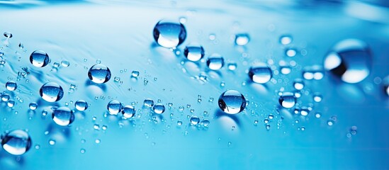 Numerous water droplets are visible on a smooth blue surface. The droplets are reflecting light, creating a dynamic and textured appearance.