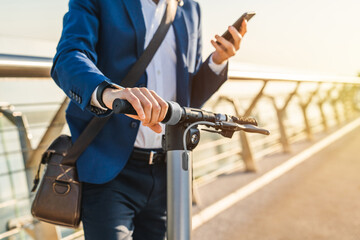 Cropped image of businessman using phone on his electric scooter. Closeup photo of man in business formal attire unlocking e-scooter in mobile application