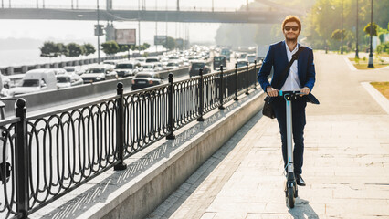 Portrait of young business man riding electric scooter on road in city. Caucasian attractive manager lawyer employee using ecological transport on the way to work