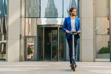 Young man in suit driving his scooter near business center at sunny day. Businessman riding using e-transportation outdoors in the street