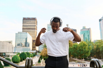 stylish young african american man listening to music with headphones outdoors and dancing