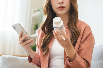 Health care asian young woman using smart phone for reading, searching prescription on bottle medicine, pill label text about information online, instructions side effects, pharmacy medicament concept