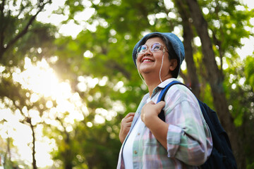 Elderly woman smiles happily Wear a hat and carry a backpack to travel in nature. Elderly tourists....