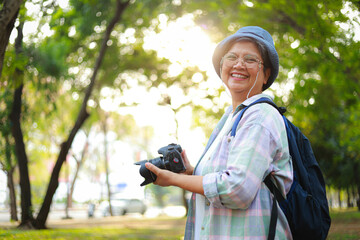 Elderly woman travels nature smiling happily Wear a hat and a backpack and carry a camera. Elderly...