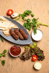 Top view of delicious kebabs lula lamb kebab with grilled vegetables and herbs on a wooden table.