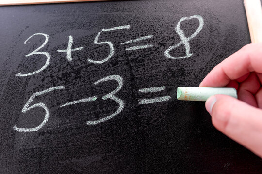 closeup teacher write simple math addition of chalkboard, primary school