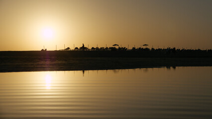 Liegen und Sonnenschirme im Gegenlicht der Abendsonne am Starnd mit Wasser im Vorderund