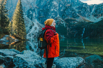 Lady tourist with a backpack standing on top of the mountain and enjoy the beautiful view of mountains Morskie Oko lake. Hiking travel and adventure in Poland, Tatry  - obrazy, fototapety, plakaty