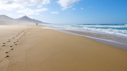 Fototapeta na wymiar 2 Wanderer am Strand von Cofete mit Dunst und Wellen und Sonnenschein