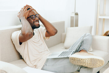 Smiling African American Freelancer Working on Laptop in Modern Home Office The young man in casual...