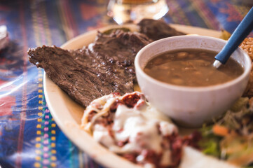 Arrachera accompanied by beans, salad, rice, chorizo and nopales, served on a white plate.