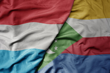 big waving national colorful flag of comoros and national flag of luxembourg .
