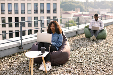 Successful business woman dressed in denim shirt and pants sitting at chair bag on roof top...