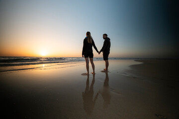 Pareja cogida de la mano mirando la salida del sol en la playa