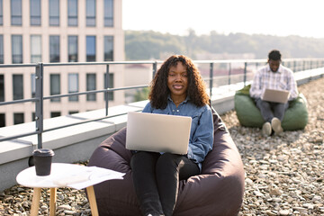 Attractive African American female freelancer using portable computer for remote work at roof top...