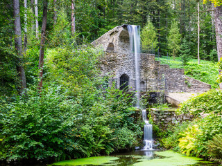 Beautiful water cascade and waterfall between trees in big green garden.