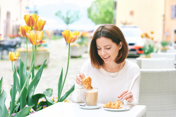 Portrait of happy mature woman having coffee with croissant in outdoor cafe - 745993723