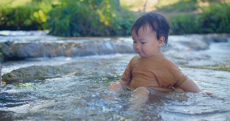 Exuberant toddler splashing in a shallow stream, laughter sparkling as sunlight filters through green foliage in a blissful outdoor scene