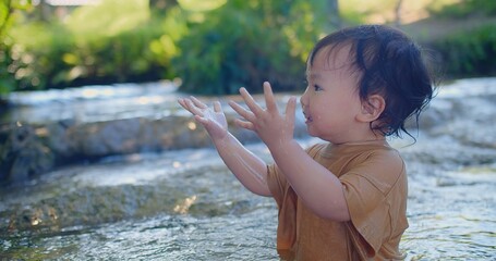 Exuberant toddler splashing in a shallow stream, laughter sparkling as sunlight filters through green foliage in a blissful outdoor scene