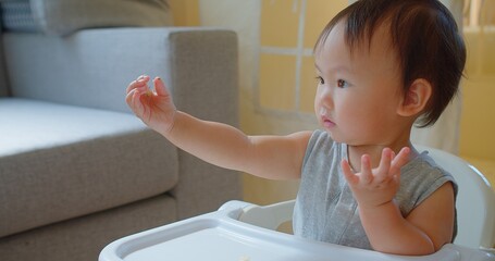 A cheerful toddler enjoys mealtime in a high chair, reaching out towards food with a bright,...
