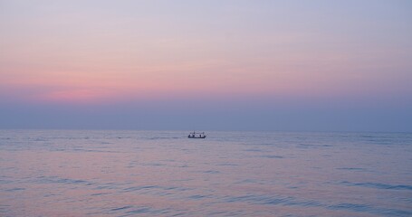 A serene twilight sunset scene over a calm ocean with a small silhouette of a distant fishing boat against the colorful pastel sky, Silhouetted Fishing Boat at Sea during a Tranquil Sunset