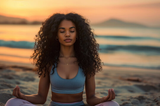 A young black woman with long curly hair doing yoga on the beach
