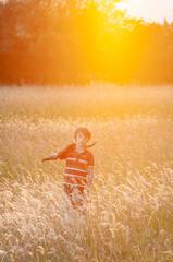 Young boy walking through meadow at sunset