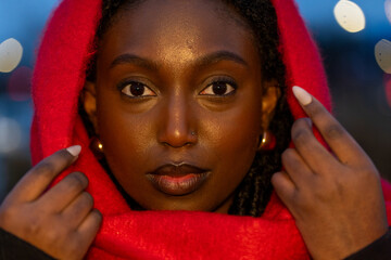 The image presents a frontal view of a self-assured young woman holding a striking red scarf up to...