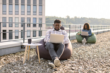 Successful business man dressed in denim shirt and pants sitting at chair bag on roof top outdoors...