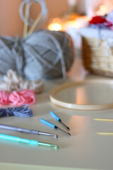 Balls of yarn, threads, various needlecraft needles and lit candles on the table. Hygge at home. Selective focus.