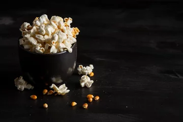 Rolgordijnen Top view of black bowl with popcorn on dark table with popcorn, grains and salt, horizontal, with copy space © Arantxa Forcada