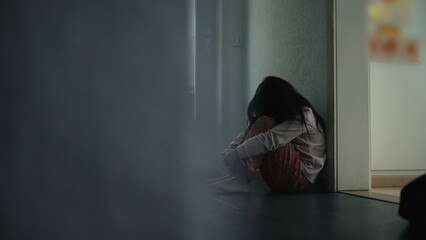 Child Struggling with Mental Illness in Childhood, Seated in Dark Home Corridor Covering Face in...