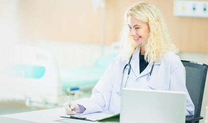 Beautiful and professional female doctor using laptop computer, working at her desk in the doctor's...