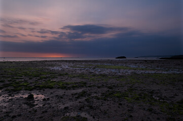 Anochecer con sol detras de las nubes y luces rojizas i violetas con algas verdes en Ujung Genteng, Sukabumi, Java, Indonesia