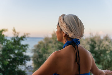 Close-up of beautiful woman with bare back and blue sarong enjoying beautiful views of the Aegean Sea between the trees at sunset in southern Crete