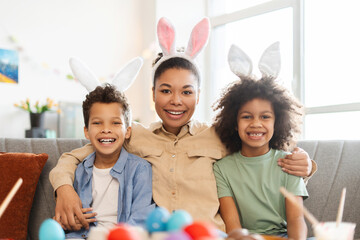 Portrait smiling mother with kids wearing bunny ears looking at camera. Happy African American family hugging celebrate Easter at home  - Powered by Adobe