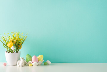 Easter decor idea: A side view of a tabletop displaying a shell-inspired planter with tulips and grass, a ceramic hare, and multicolored eggs in holder, all against a pastel turquoise wall - obrazy, fototapety, plakaty