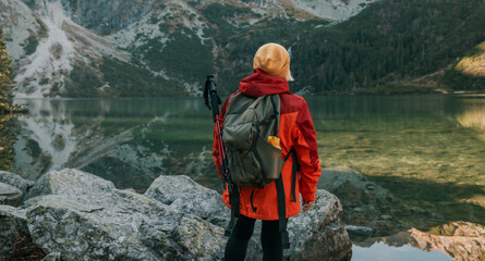 Lady tourist with a backpack standing on top of the mountain and enjoy the beautiful view of mountains Morskie Oko lake. Hiking travel and adventure in Poland, Tatry  - obrazy, fototapety, plakaty