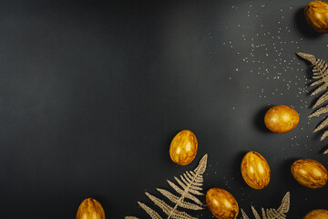 Golden and silver Easter eggs and gold branches on black table background, top view