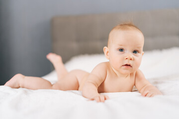 Closeup portrait of calm adorable infant baby lying on bedroom bed, enjoying morning relaxation indoor at home, looking at camera. Carefree healthy babyhood, healthcare and pediatrics care concept.