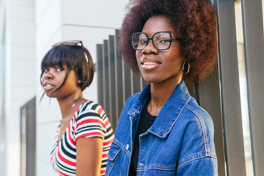 African American sisters in casual wear engage with urban surroundings, their close bond evident in their comfortable expressions