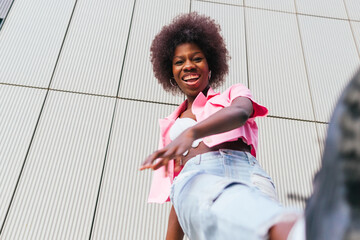 From below of joyful young woman laughing candidly, her vibrant pink shirt and casual denim creating a perfect blend of urban chic and carefree spirit