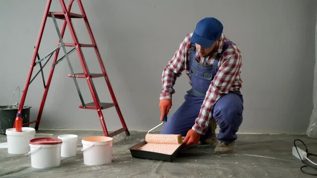Concentrated handyman is preparing paint roller for work. Professional interior construction worker