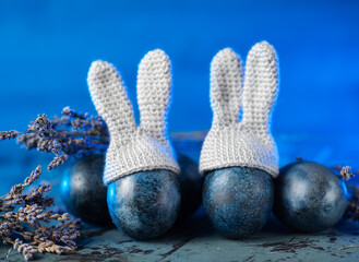 Blue Easter eggs with bunny ears on a blue table. Lavender flowers. Knitted Bunny Hats