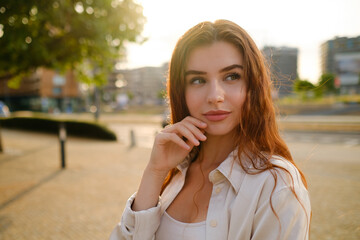 Mysterious red haired girl stands in the park at sunset. 