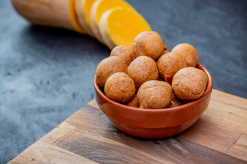 Pumpkin Fritters. Composition where the fritters are in a bowl on a table with the pumpkin out of focus.