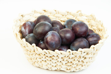 round blue plums in a basket on a white background. ripe sweet plums on a light texture	