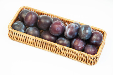 round blue plums in a basket on a white background. ripe sweet plums on a light texture	